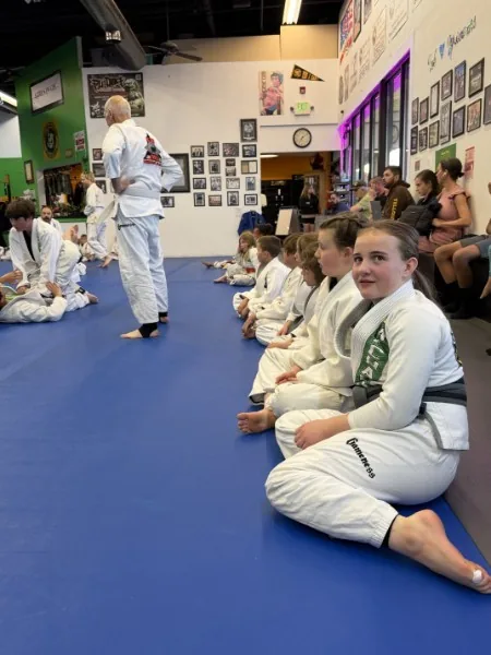 Kids seated in line on the mat, the girl at the front smiling