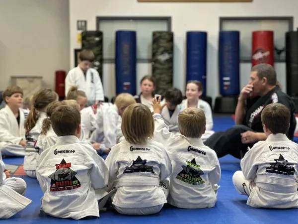 Kids in Team Fujii gis seated on the mat listening to their instructor