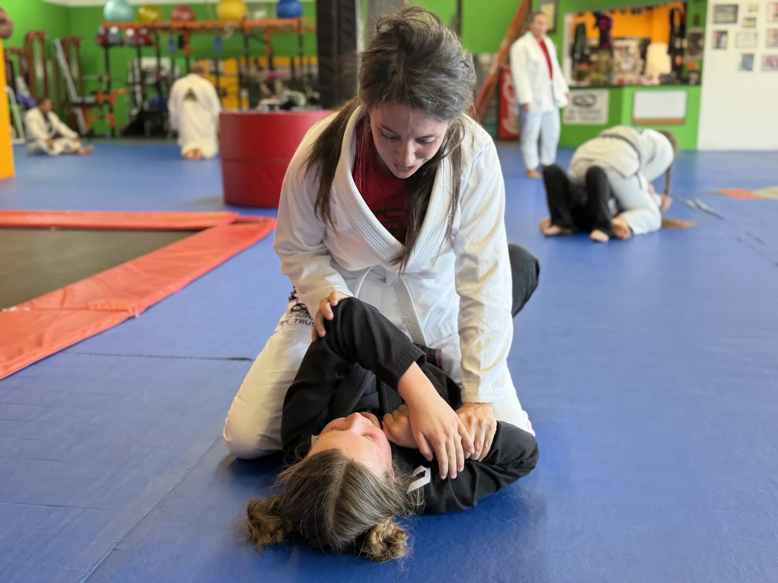 Two women training Brazilian Jiu-Jitsu on the mat, working positional control from the ground